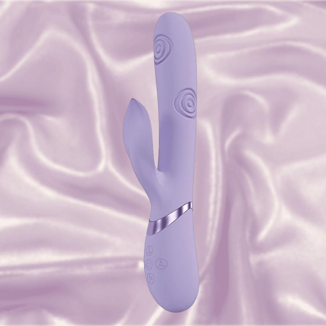 The Dolce Vive Fronda Rechargeable G-Spot Vibrating and Tapping Leaf Clit Stim by Shots America, in lavender, features a swirled shaft for G-Spot stimulation and a leaf-shaped clitoral stimulator, displayed on silky light purple fabric.