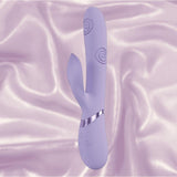 The Dolce Vive Fronda Rechargeable G-Spot Vibrating and Tapping Leaf Clit Stim by Shots America, in lavender, features a swirled shaft for G-Spot stimulation and a leaf-shaped clitoral stimulator, displayed on silky light purple fabric.