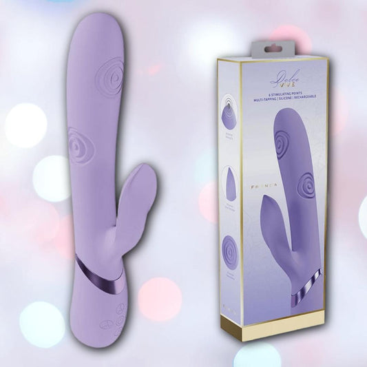 A purple Dolce Vive Fronda Rechargeable G-Spot Vibrating and Tapping Leaf Clit Stim by Shots America, with a curved silicone design and control buttons, appears next to its box featuring product imagery on a blurred pastel background. 1080