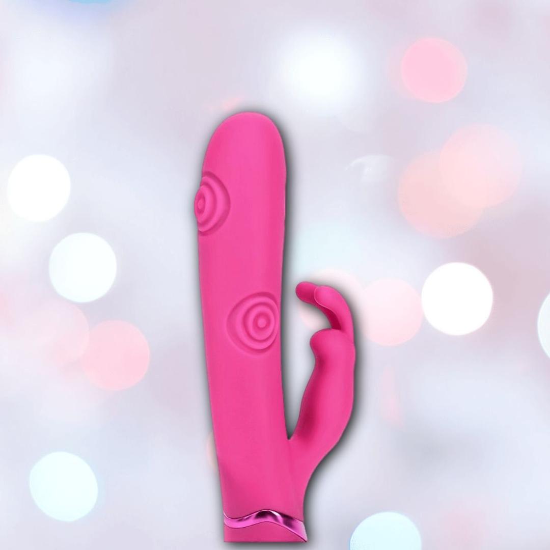 The Shots America Dolce Vive Mimi Rechargeable G-Spot Vibrating and Tapping Rabbit-Pink features textured spiral patterns and a curved extension, displayed against a soft pastel bokeh background.