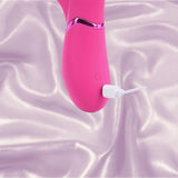 The Dolce Vive Mimi Rechargeable G-Spot Vibrating and Tapping Rabbit in pink by Shots America is being charged with a white cable, resting on a light purple satin fabric background.