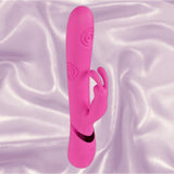 The Shots America Dolce Vive Mimi Rechargeable G-Spot Vibrating and Tapping Rabbit in pink, featuring dual stimulation arms and a spiral texture, stands upright on soft light purple satin fabric.