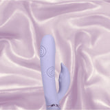 The Dolce Vive Pallina Rechargeable G-Spot Vibrating and Tapping Beads Clit by Shots America, in lavender, featuring textured rings and a curved extension, is displayed on light purple satin fabric.