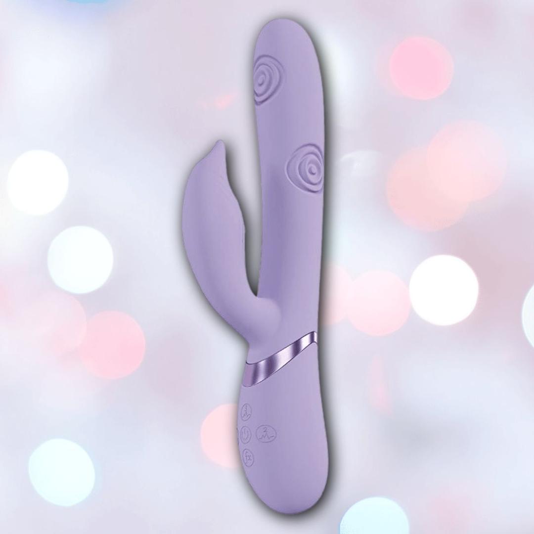 The Shots America Dolce Vive Pallina is a lavender rechargeable G-spot and clit vibrator with a curved shaft, textured spiral patterns, silver accents, and set against a soft pastel bokeh background.