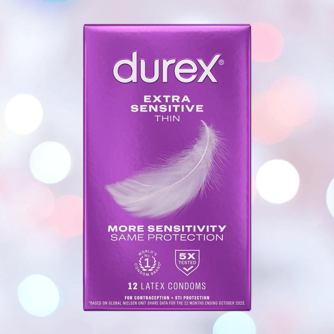 A purple box of Durex Extra Sensitive 'Thin' Condoms features a feather graphic for "more sensitivity, same protection." Includes 12 extra lubricated thin latex condoms. The soft, blurred background shows gentle light circles.