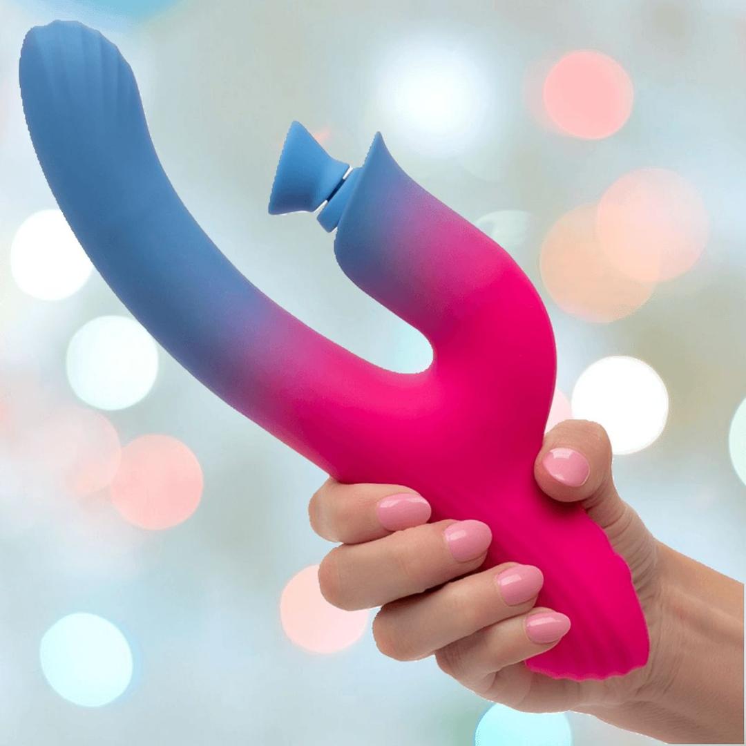 A manicured hand holds the CalExotics Elation Dual Stimulator with Suction, a colorful blue and pink gradient silicone vibrator, against a softly blurred background.