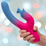 A manicured hand holds the CalExotics Elation Dual Stimulator with Suction, a colorful blue and pink gradient silicone vibrator, against a softly blurred background.