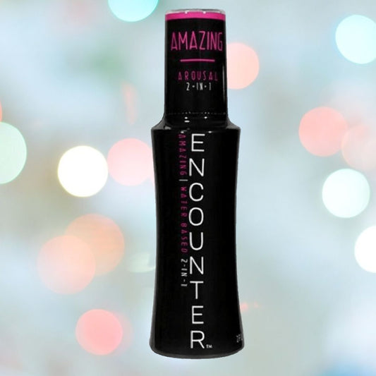 A bottle of Encounter "Amazing" Water-Based Lubricant | 2oz is showcased against a blurred background featuring multicolored bokeh lights. Its packaging, predominantly black with pink accents, subtly suggests its Arginine-infused formula crafted to enhance pleasure. 1080