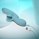 The Evolved Take Your Flick, a blue silicone flickering vibrator by Evolved Novelties with a split tip, charges via a white USB cable against a soft blue and white background with gentle abstract lighting, promising customizable pleasure.