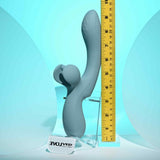 The Evolved Take Your Flick by Evolved Novelties, a gray silicone dual-prong flickering vibrator, stands upright on a clear "EVOLVED" stand by a yellow ruler showing its 8-inch length. The background is teal.