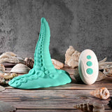The Evolved Tentacle Grinder by Evolved Novelties, a turquoise suction-cup toy, stands upright on wood amid seashells. Next to it is a white three-button remote for customizable vibrations, set against a gray textured wall.