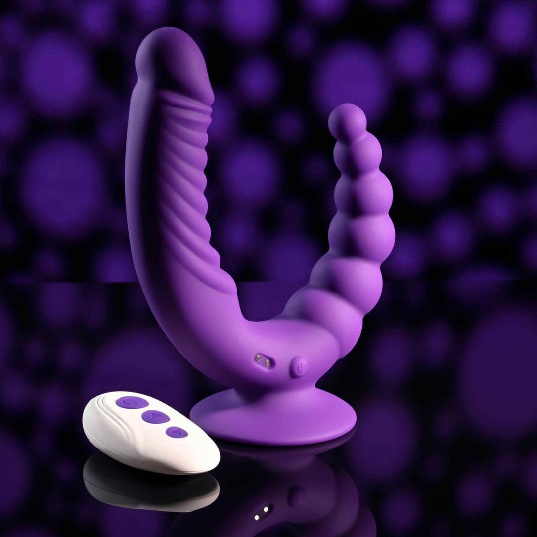 The Evolved The Rider by Evolved Novelties is a purple double-ended vibrator with a ribbed shaft, beaded end, suction base for hands-free use, and a white remote with purple buttons, shown on a blurred purple background.