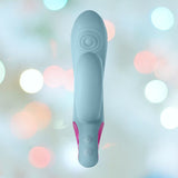 A top-down angle showcases the sleek design of the Femme Funn Cora Rabbit Vibrator - Light Blue, featuring ergonomic curves and pink accents on the sides. The soft focus background with blurred pastel-colored circles highlights its elegant style. Near the top, circular patterns add to its sophistication while the device offers ten powerful vibrating modes for an enhanced experience.