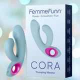 A box titled "Femme Funn Cora Rabbit Vibrator - Light Blue" features an image of the product depicting a light blue, ergonomic vibrator with pink accents. The background is blurred with pastel colors, adding a soft, dreamy effect. Enjoy powerful vibrations and ten vibrating modes with this luxurious device from Femme Funn.