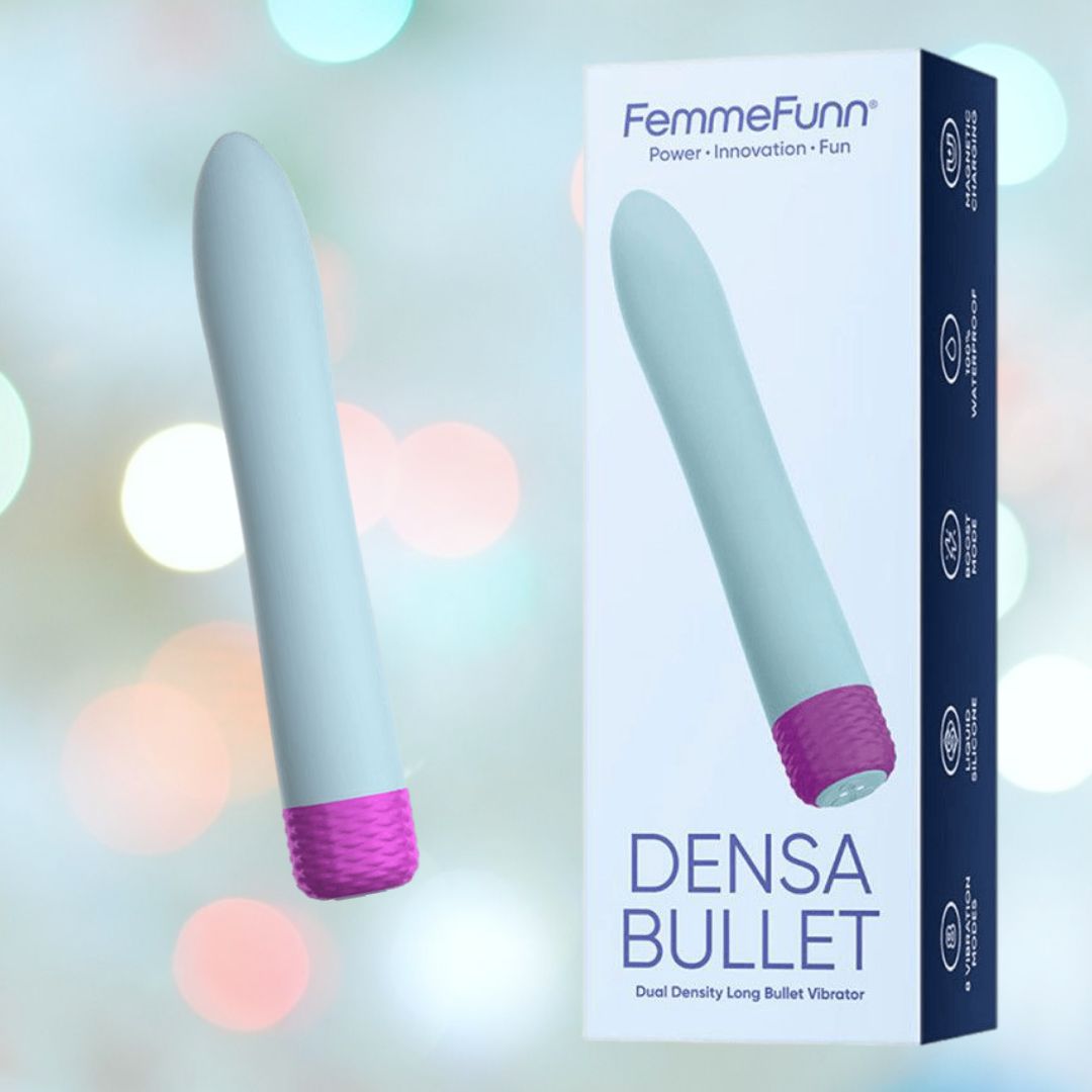 Image shows a Femme Funn Densa Bullet Vibrator - Light Blue against a soft, blurry background with light spots. The vibrator, featuring a long slim design, powerful motor, and a light blue textured grip end, is displayed next to its packaging box which also shows an image of the product.