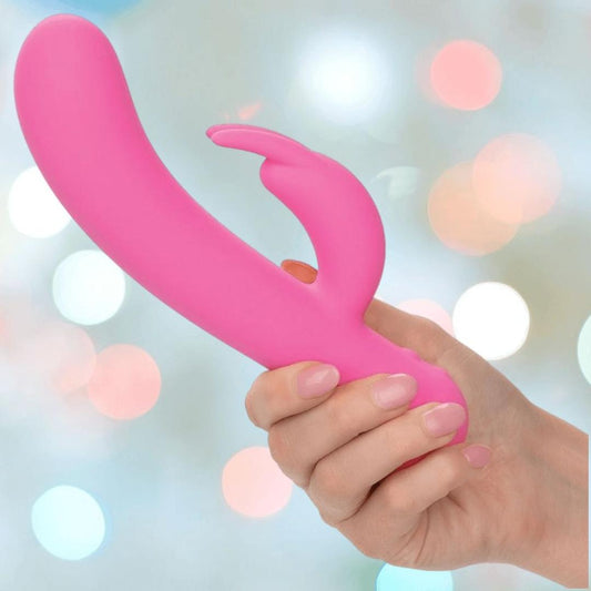 A hand holds the CalExotics First Time Rechargeable Bunny with Turbo Boost Accelerated Speeds, set against a softly blurred pastel background, hinting at powerful dual stimulation and intense pleasure. 1080