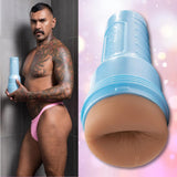 A tattooed man with a mustache, wearing pink underwear, stands in a shower holding the Fleshlight Fleshjack Boys Boomer Banks Realistic Male Masturbator Cake Butt. Beside him is a close-up of the product against a softly lit pink background.