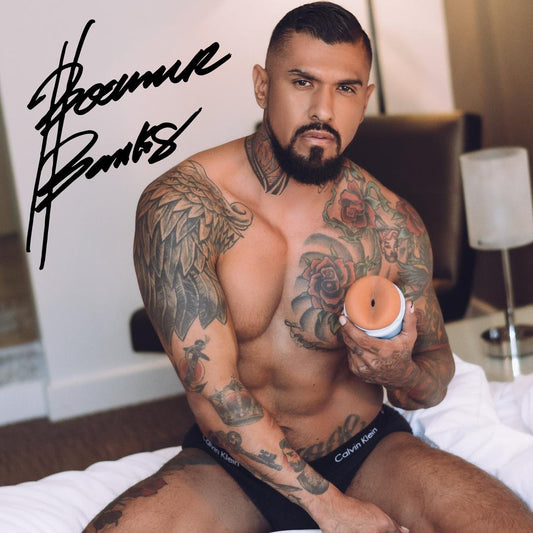 A muscular, tattooed man with a beard sits on a bed in Calvin Klein underwear, holding a Fleshlight Fleshjack Boys Boomer Banks: Realistic Male Masturbator Cake Butt. A large black signature is visible at the top left of the image. 1080
