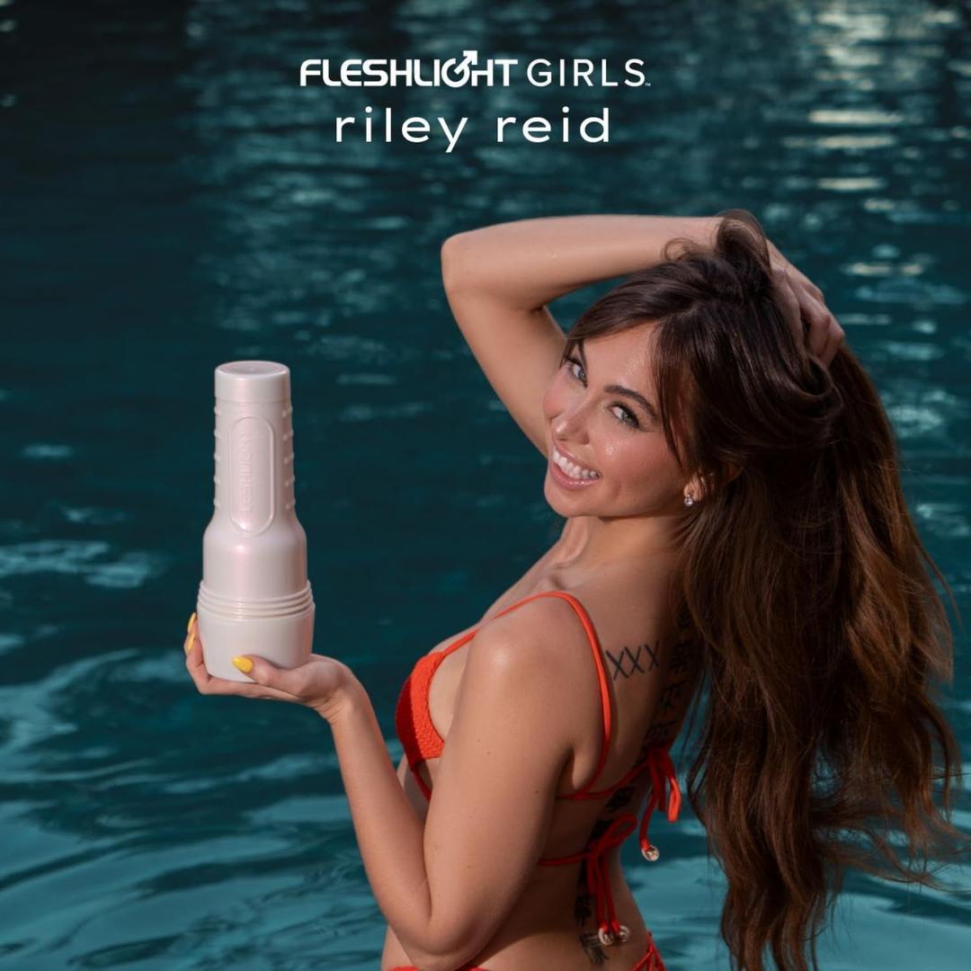 A woman in a red bikini smiles by a pool, holding a Fleshlight Girls: Riley Reid Utopia from Fleshlight. The text above her reads "Fleshlight Girls: Riley Reid Utopia.