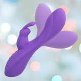 The CalExotics Flex Bend & Hold Double Rumbler Rabbit Vibrator—a purple silicone vibe with curved extensions and a butterfly-inspired design—provides dual stimulation for heightened pleasure, set against a soft pastel bokeh background.