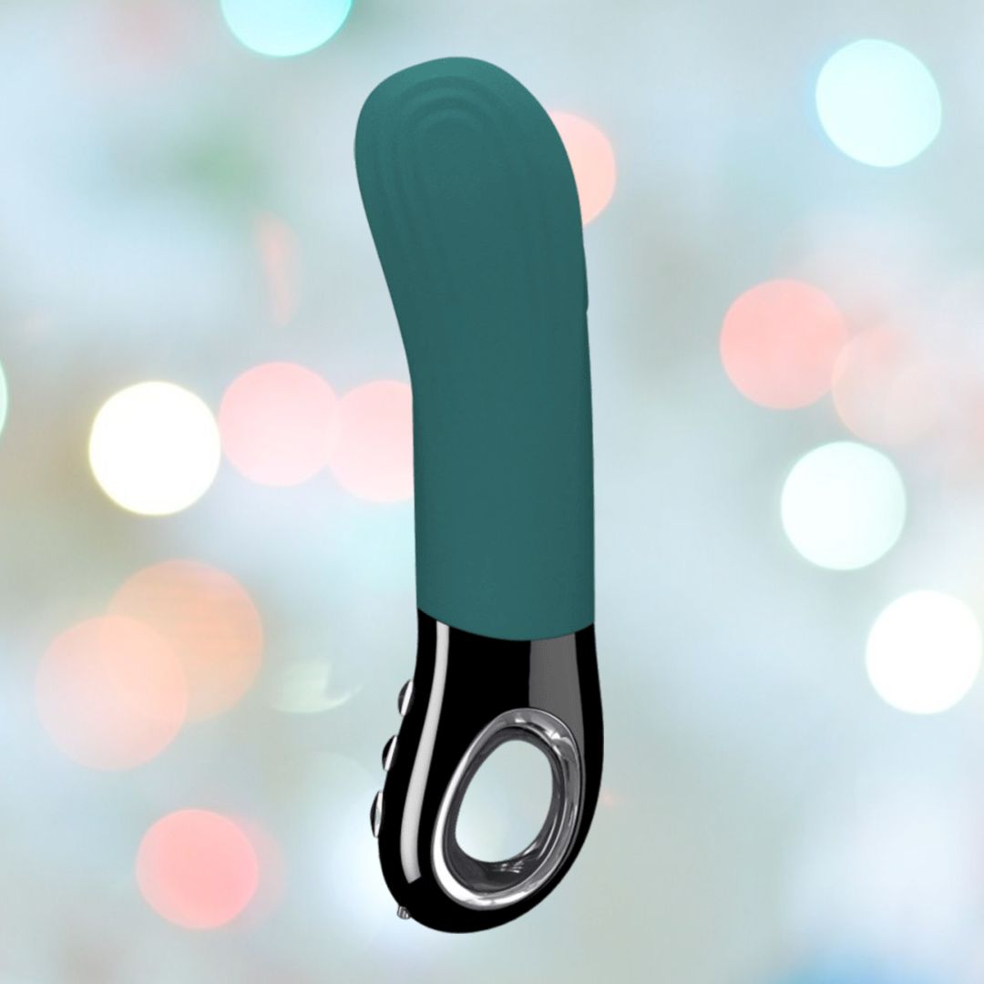 The Fun Factory Manta Rechargeable Vibrating Male Stroker For Men in Deep Blue is a sleek and modern device featuring a looped handle and silver accents. It is showcased against a soft, bokeh background of blurred lights in shades of white, pink, and blue.