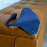 A blue, stingray-shaped silicone toy with textured ridges from Evolved Novelties’ Gender X Daily Grind rests on a tan tufted leather bench—a body-safe pleasure product.