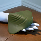 The Gender X Pleasure Pad by Evolved Novelties is a silicone, olive green pleasure device with raised ridges, shown on a white mannequin hand on brown leather. The gender inclusive pad features the "GENDER" branding.