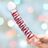 A hand holds the Gläs 10" Mr. Swirly Spiral Glass Dildo, featuring a distinctive red spiral design, against a blurred backdrop with soft, circular lights in an array of colors.