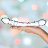 A hand holds a dual-ended glass object with a coiled design in the center, aptly named the Gläs 10" "Double Trouble" Double-Sided Glass Dildo. The background is blurred with circular, multicolored lights that enhance the allure of this perfect tool for G-spot massage.