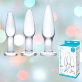 Three frosted glass anal plugs of different sizes are lined up against a soft, blurred pastel background, ideal for backdoor exploration. To the right is a box labeled "Gläs 3 Piece Anal Training Set," showcasing this luxurious glass set crafted by Gläs for ultimate anal pleasure.