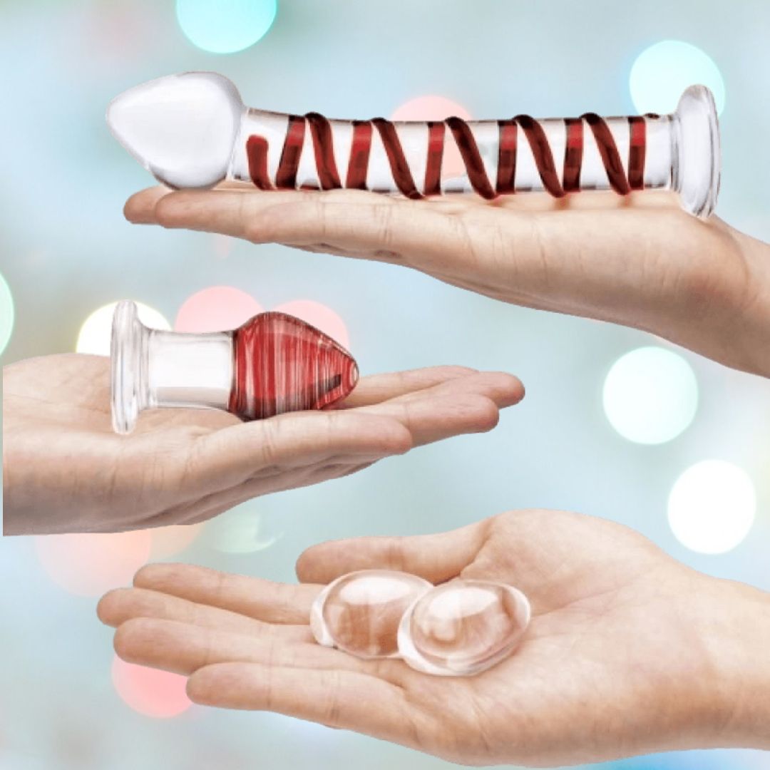 Hands hold three glass objects against a blurred backdrop with colored lights: a long cylindrical piece with a spiral pattern similar to the Gläs Mr. Swirly Glass Dildo and two smooth oval forms like Kegel Balls, each highlighting unique artistry.