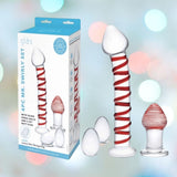 Against a bokeh-lit backdrop, the Gläs 4pcs Mr. Swirly Set is showcased, featuring a Mr. Swirly Glass Dildo with a red spiral, two round kegel balls, and an elegant butt plug. The packaging highlights these exquisite items with detailed descriptions.