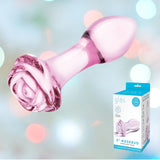 A pink glass anal toy with a rose-shaped base is showcased against a background featuring a soft, blurred gradient of pastel colors. A product box beside it displays the brand "Gläs" and describes it as the "5” Rosebud Glass Butt Plug," ideal for experimenting with temperature play.