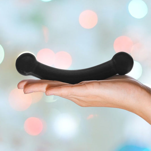 A hand holding the Gläs 5.5" Double Bull Black Glass Dildo, a sleek and hypoallergenic object, against a blurred background adorned with soft lights. 1080