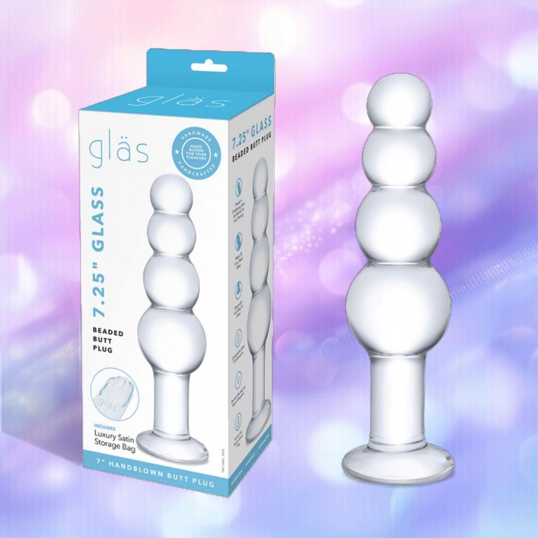 The Gläs 7.25" Glass Beaded Butt Plug by Gläs, made of body-safe glass with three rounded bulbs, is shown next to its blue and white branded packaging on a purple background with bokeh light effects.