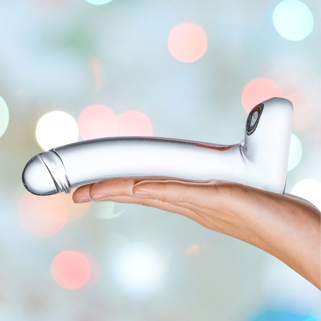 A hand holds the Gläs 7" Realistic Curved Glass G-Spot Dildo, a glossy white object shaped like a long handle with a rounded end, against a blurred background of colorful lights.