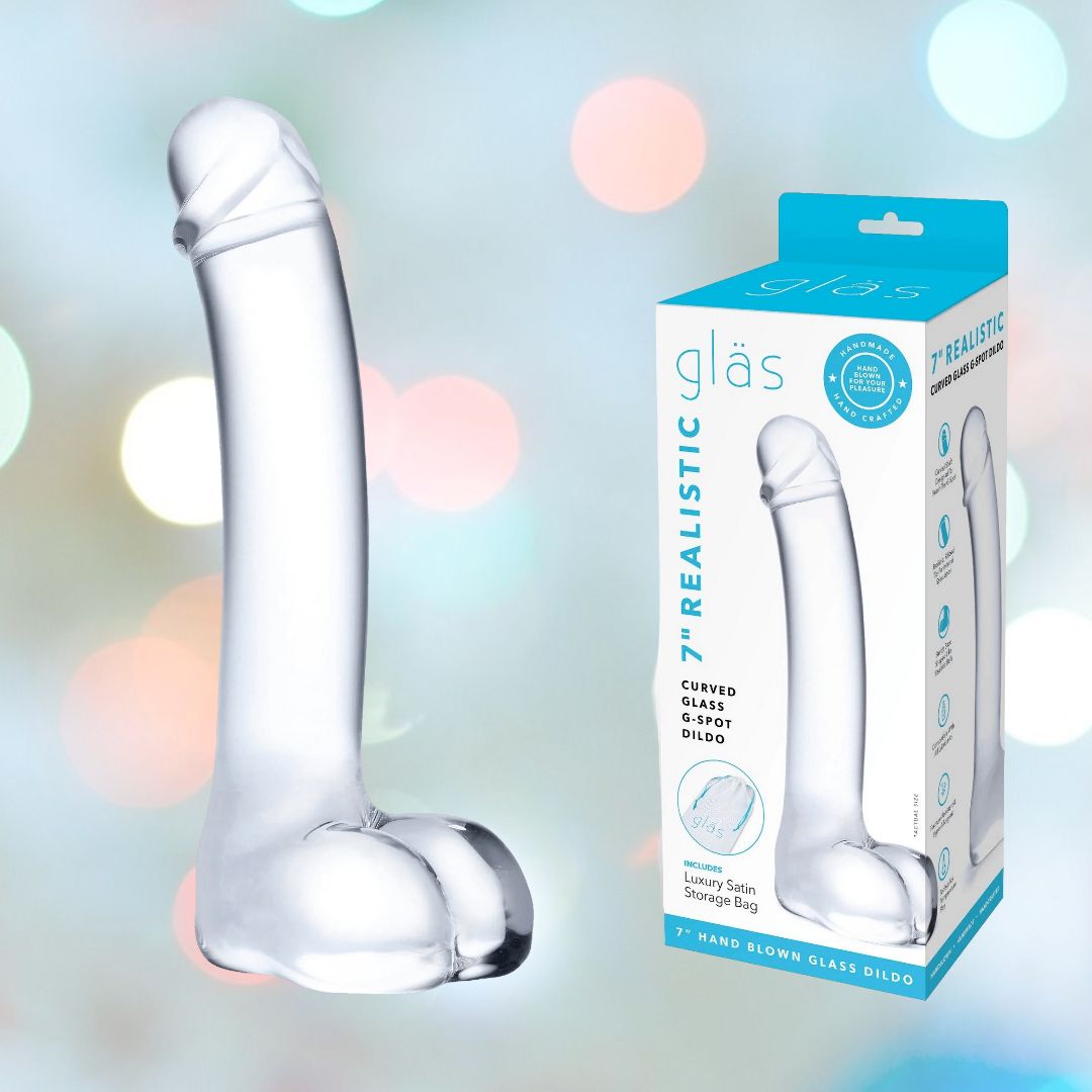 A Gläs 7" Realistic Curved Glass G-Spot Dildo, crafted from transparent and fracture-resistant glass, sits next to its packaging labeled "Gläs." Designed for temperature play, it is set against a backdrop of soft, colorful bokeh lights.