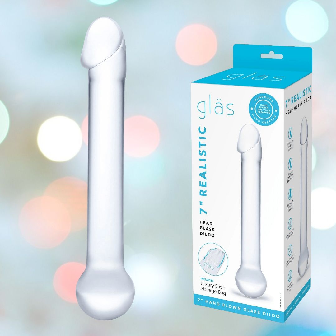 A packaging box displays the Gläs 7" Realistic Head Glass Dildo, ideal for temperature play, featuring a realistic head. It is elegantly positioned next to its minimalist box with blue accents. In the softly blurred background, colorful lights enhance its allure.