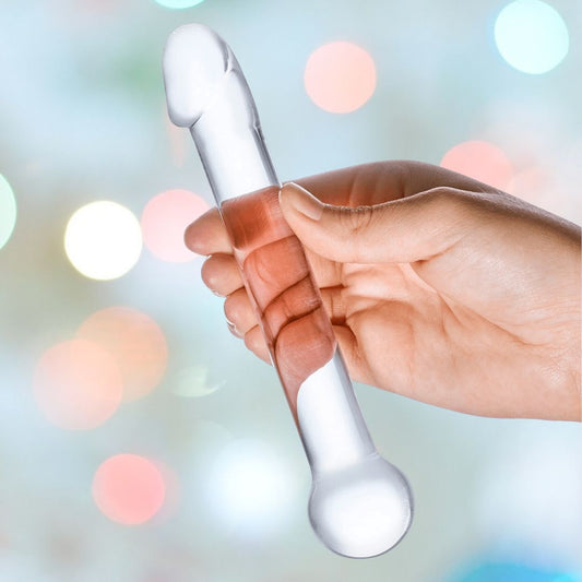 A hand holds the Gläs 7" Straight Glass Dildo, a transparent pleasure tool shaped like a rod. The background is blurred with colorful, circular lights, giving a festive appearance. 1080