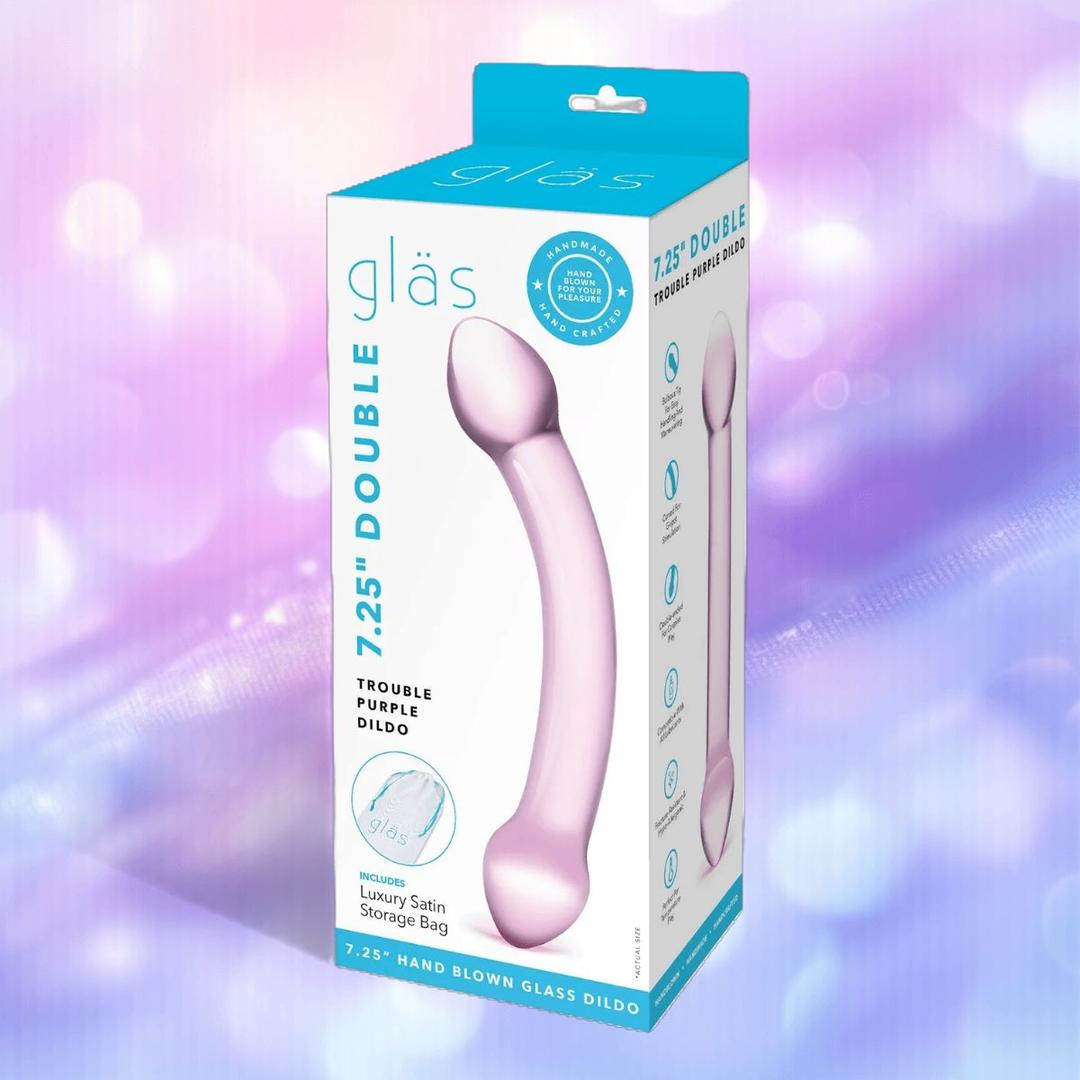 A retail box for the Gläs Double Trouble Purple Dildo by Gläs, a double ended glass toy for temperature play, is shown with product images and details on blue and white packaging against a blurred pastel background.