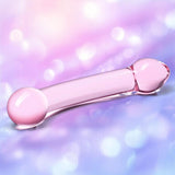 The Gläs Double Trouble Purple Dildo by Gläs, a transparent pink glass toy with rounded ends, is showcased on a soft, blurred purple and pink background with bokeh light effects.