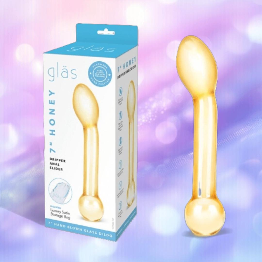 The Gläs Honey Dripper 7" Double Ended Anal Dildo and its box, branded by Gläs, are shown against a pastel, blurred background. The toy is clear with a golden tint and curved for G-Spot or P-Spot pleasure.