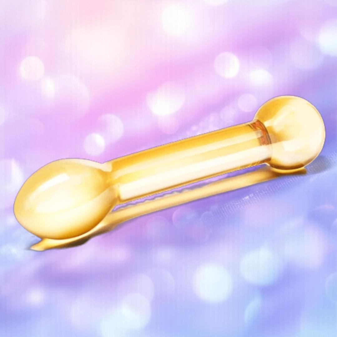 The Gläs Honey Dripper 7" Double Ended Anal Dildo by Gläs, featuring rounded yellow glass ends, lies on a soft-focus pink and purple background.
