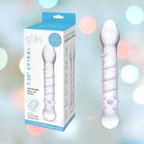 Product image of the "Gläs Spiral Staircase Full Tip G-Spot Glass Dildo." The packaging is on the left, showcasing the product name with a blue and white color scheme. The dildo itself is on the right, clear with a spiral design ideal for G-spot massage. The background features a soft focus with pastel-colored lights.