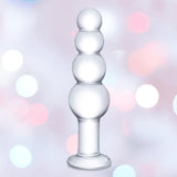 The Gläs 7.25" Luxury Glass Beaded Butt Plug by Gläs features four smooth, stacked bulbs in body-safe clear glass, displayed against a pastel bokeh background with pink and white lights.