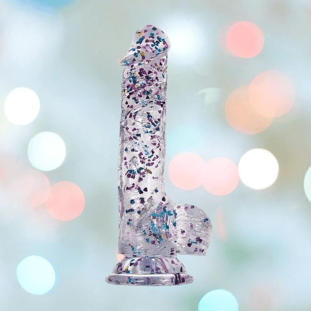 The Icon Brands Glittergasm Dong - Blue and Green Swirl 8" features colorful confetti-like flecks and stands upright against a pastel backdrop. This harness compatible dildo adds fun sparkle to your collection.