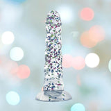 The Glittergasm Dong - Blue and Green Swirl 7" by Icon Brands stands upright, highlighting its premium silicone build, colorful swirled design, and harness compatibility against a softly blurred pastel background.
