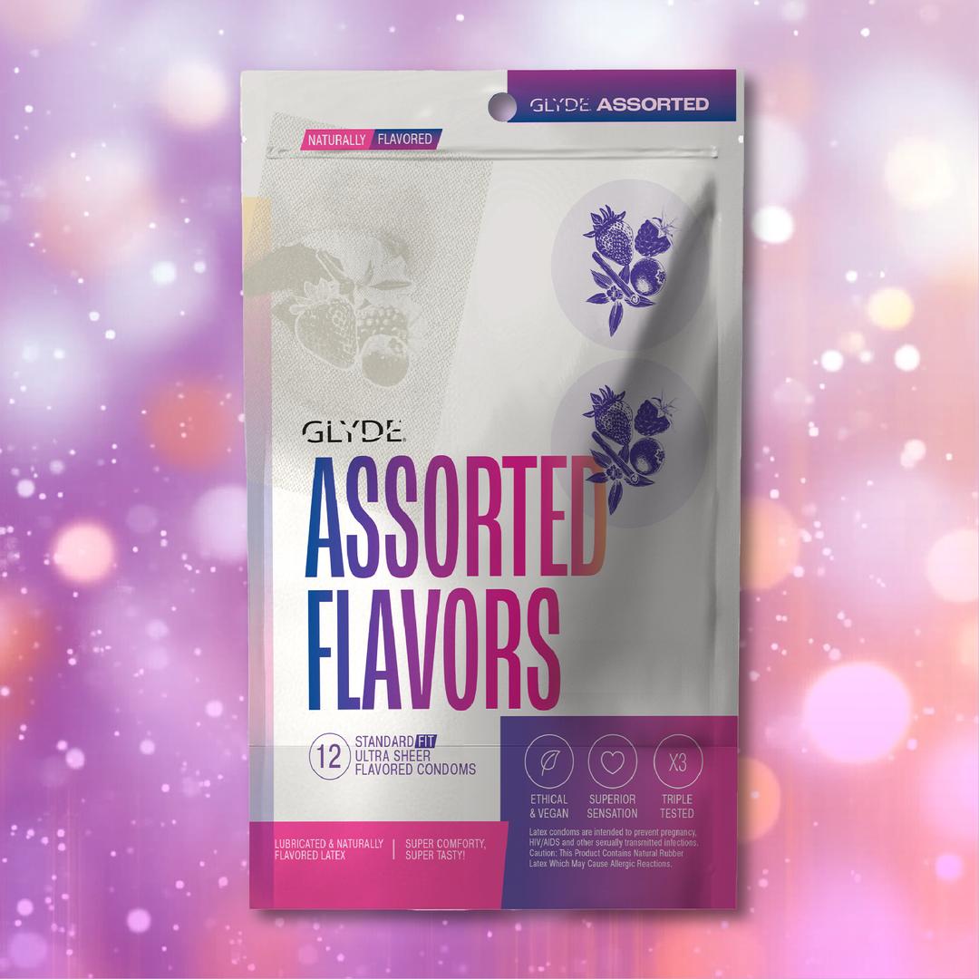 A box of Glyde Natural Flavors Condoms with 5 Flavors (12-Pack) is shown against a pink and purple bokeh background. The packaging notes they are vegan, made from natural latex, ethically produced, and triple-tested for quality.