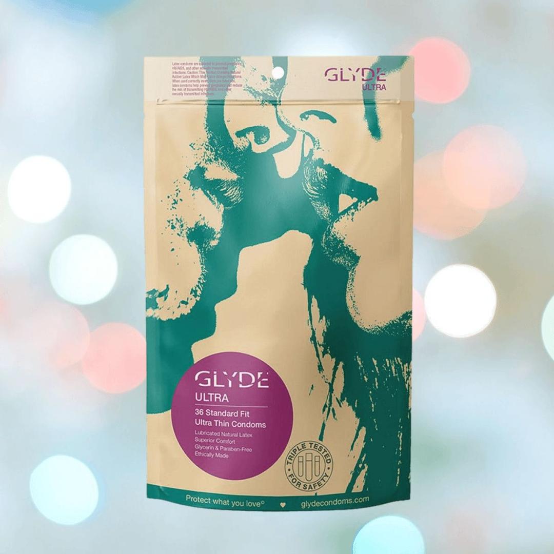A package of Glyde Ultra Super-Thin Condoms by Glyde, featuring two green face silhouettes about to kiss on a beige background with a pink label, set against a soft, pastel-colored backdrop.