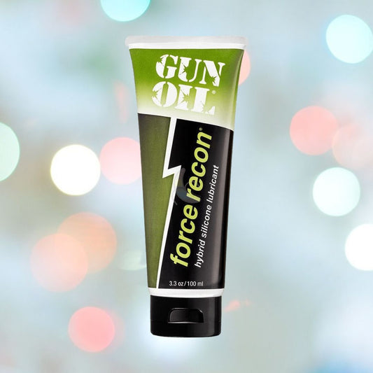 A tube of Gun Oil "Force Recon" Hybrid Lube against a blurred background with colorful bokeh lights. The green and black design featuring a lightning bolt graphic houses 3.3 oz or 100 ml of product in a leak-proof pump bottle. 1080